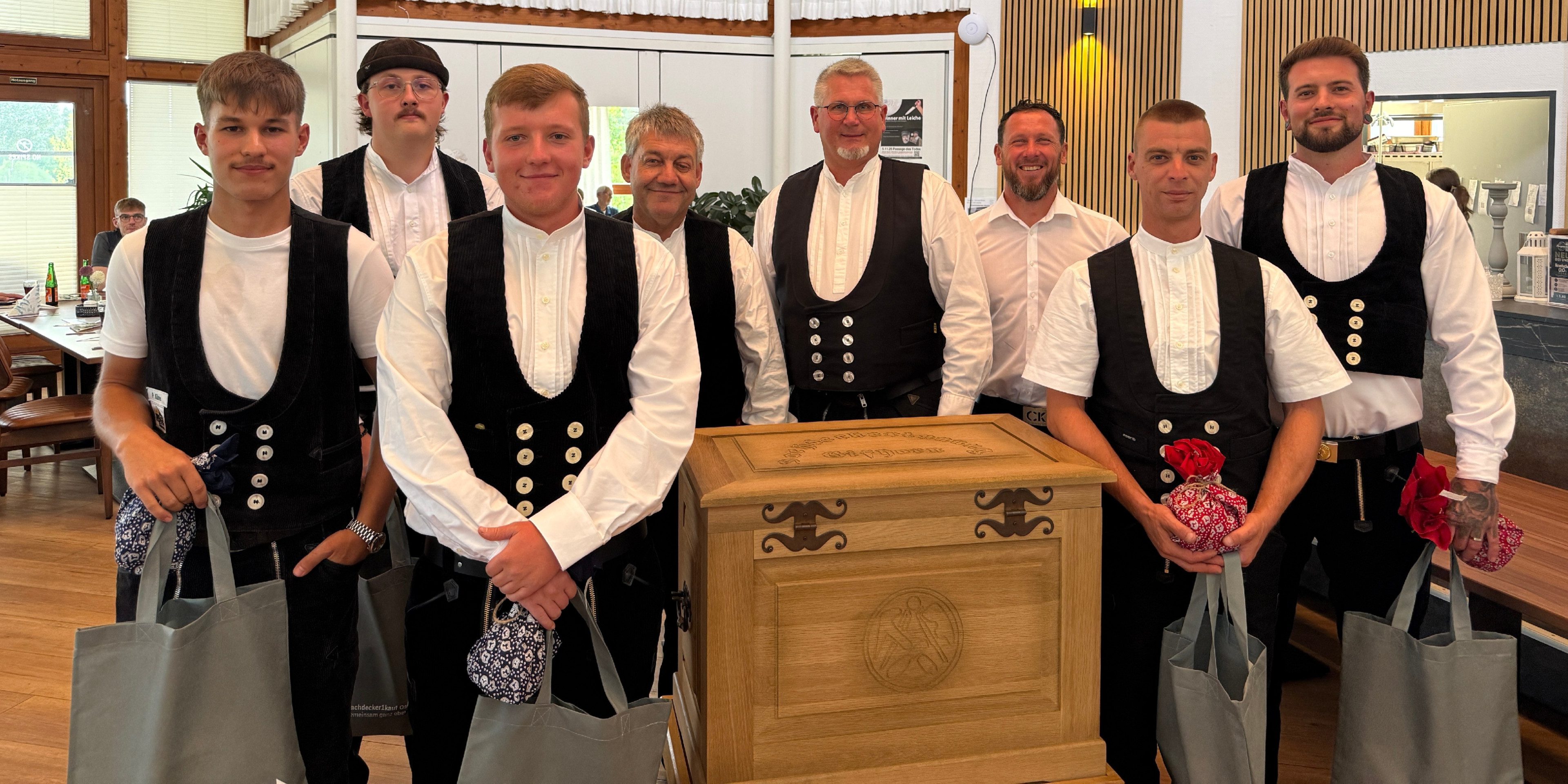 Gruppenfoto von Handwerkern in traditioneller Zunftkleidung vor einer Holztruhe