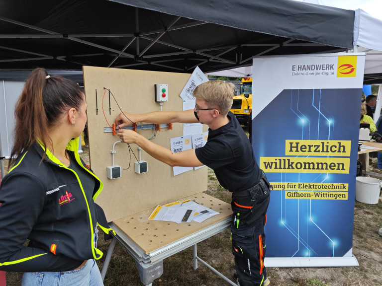Elektro-Ausbildung und praktische Übung beim E-Handwerk Gifhorn-Wittingen Elektro-Ausbildung: Zwei junge Menschen arbeiten an einer Elektrotechnik-Übungswand bei einer Veranstaltung des E-Handwerks Gifhorn-Wittingen.