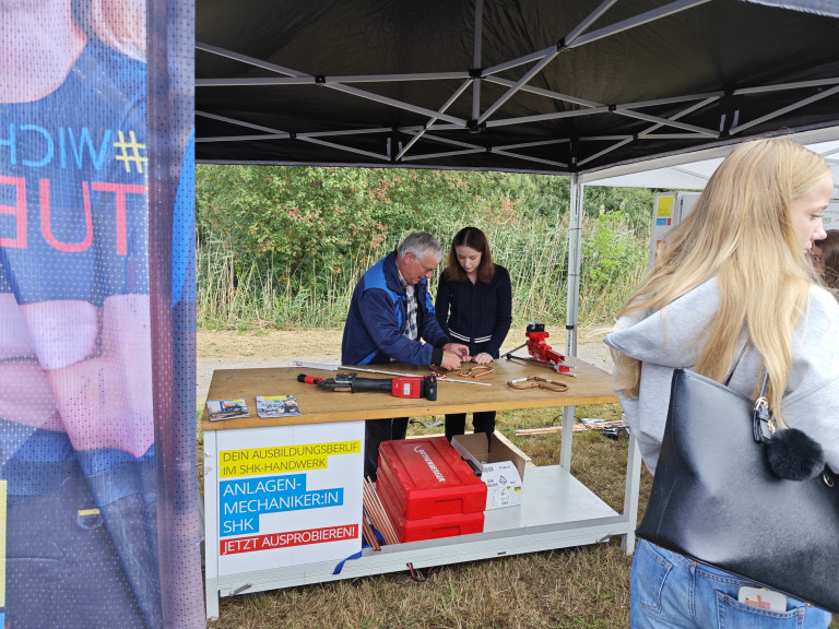 SHK-Ausbildung: Anlagenmechanikerin und Ausbilder bei praktischer Vorführung auf Berufsmesse SHK-Ausbildungsberuf: Anlagenmechanikerin und Ausbilder bei praktischer Übung auf Messe oder Infotag