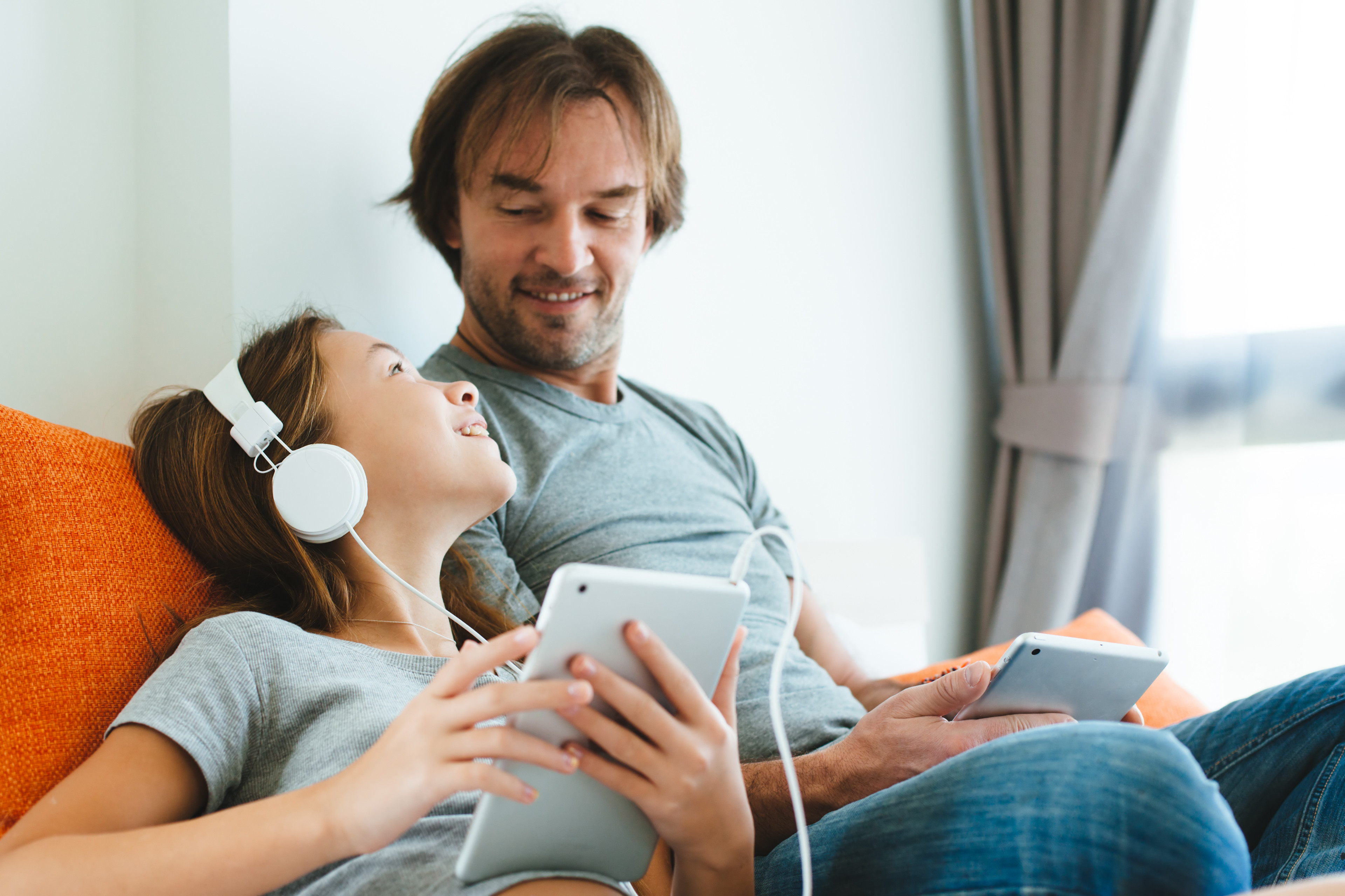 adobestock-133459851: Mann und Frau entspannt auf dem Sofa mit Tablet und Kopfhörern