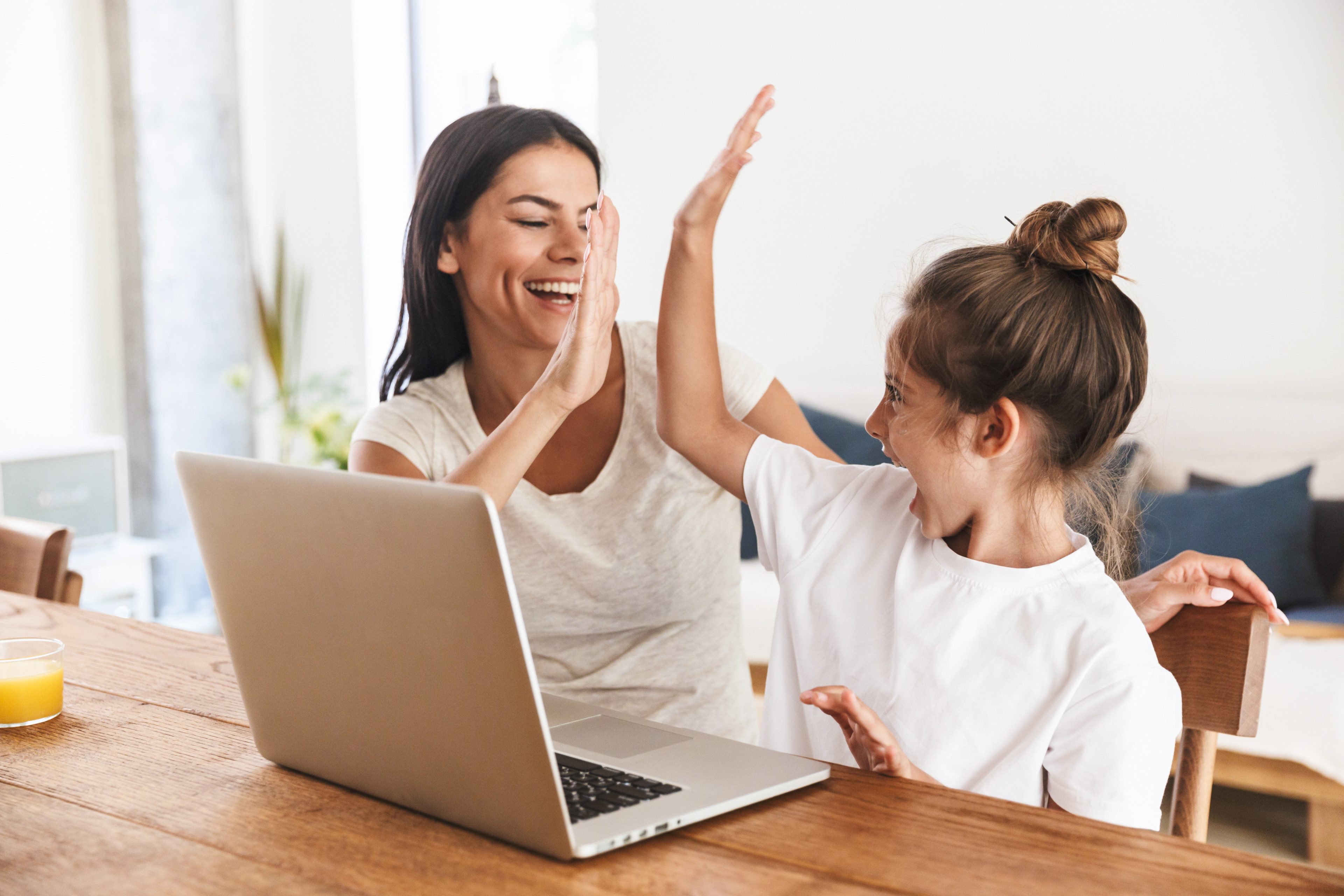 adobestock-288878265: Mutter und Tochter geben sich ein High Five beim Lernen am Laptop zu Hause