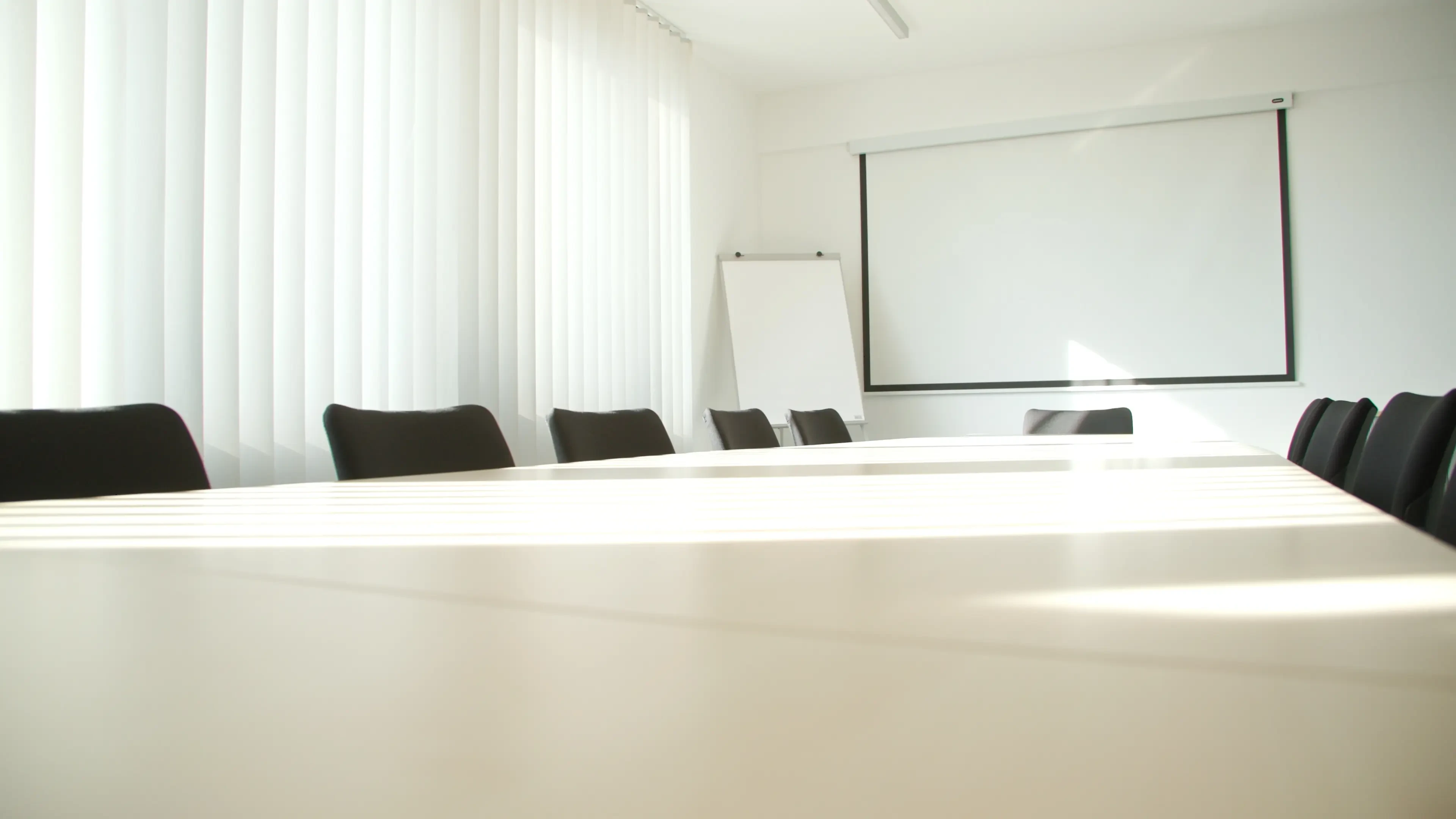 Moderner Konferenzraum mit großem Tisch, Stühlen, Flipchart und Leinwand