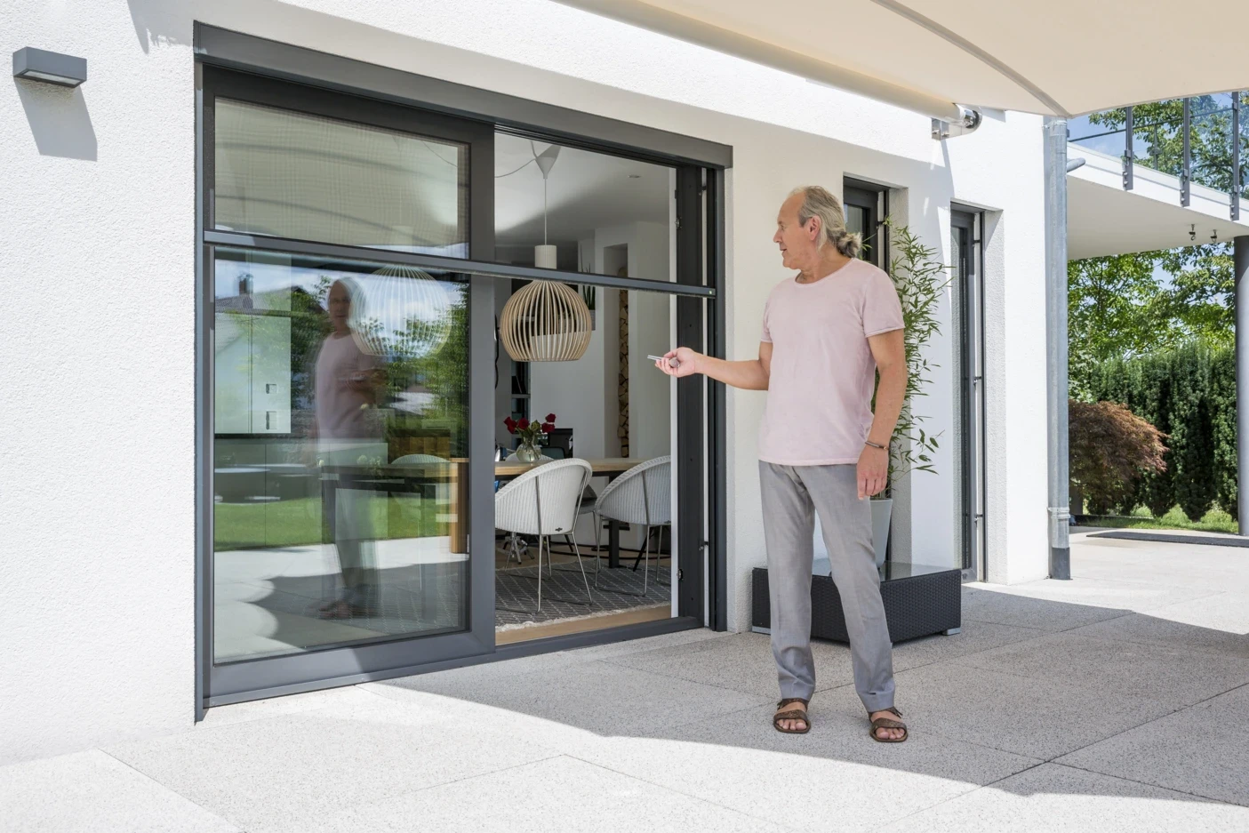 Mann öffnet große Schiebetür mit Fernbedienung auf einer Terrasse