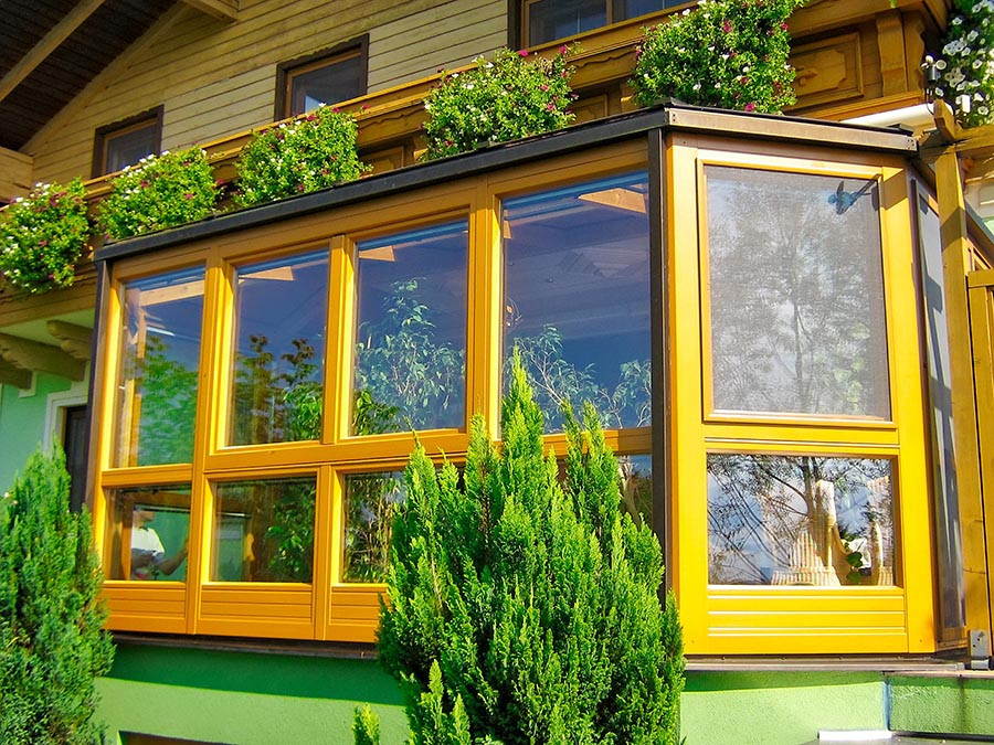 Moderner Wintergarten nachher mit gelbem Rahmen und viel Grünpflanzen vor einem Haus