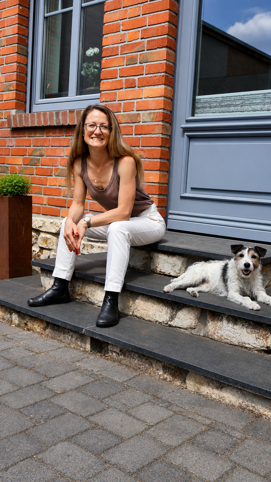 Ina Broermann, Heilpraktikerin für die Region Schönebeck, sitzt auf einer Steintreppe vor einem Haus mit Hund