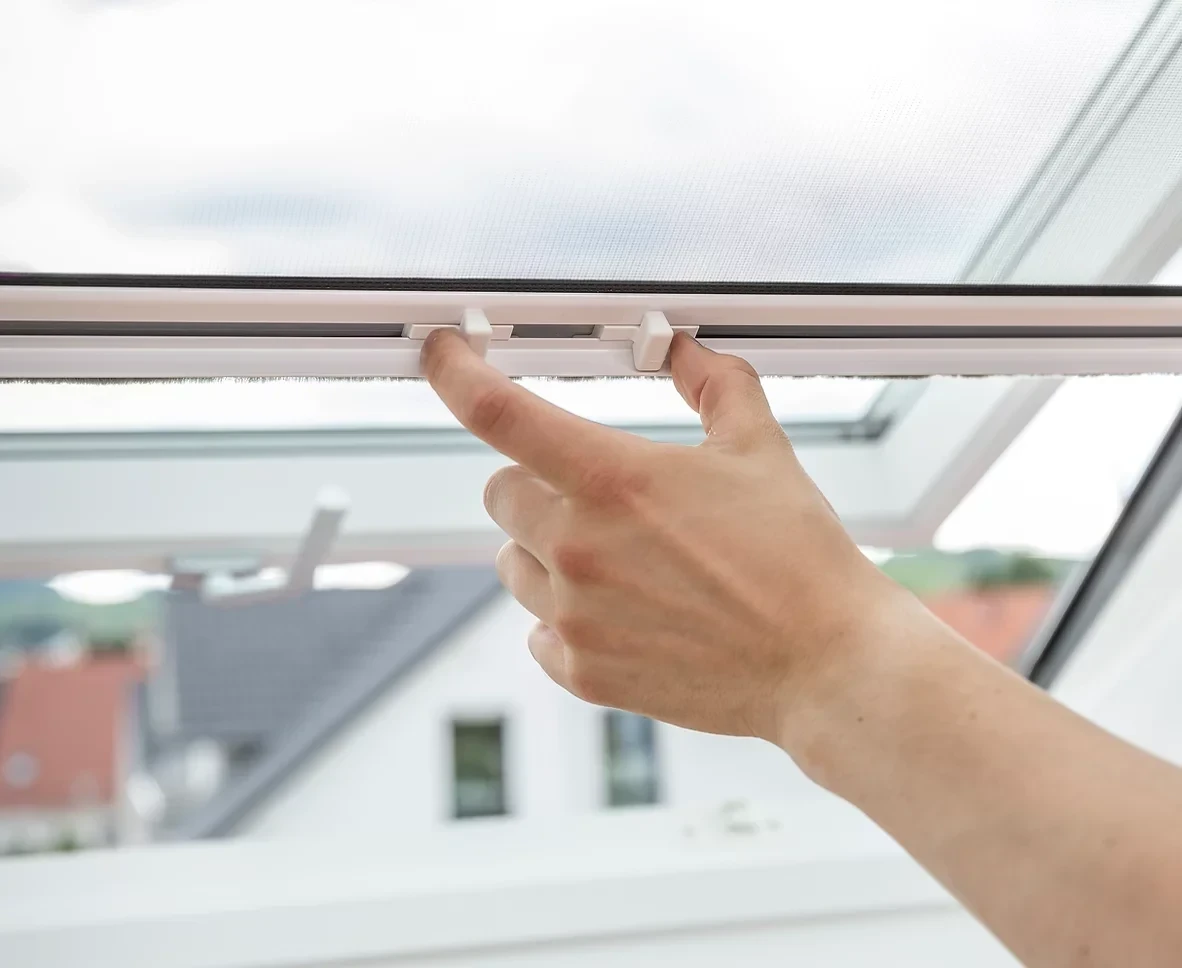 Hand justiert Insektenschutz an einem geöffneten Fenster