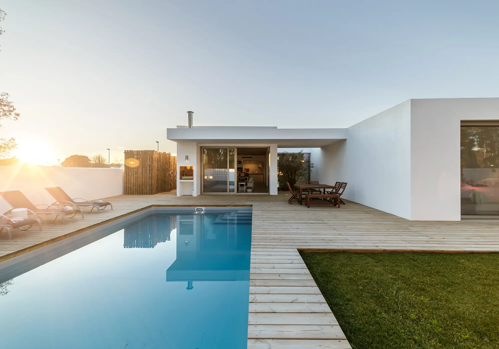 Moderner Pool im Garten mit Holzterrasse und Lounge-Bereich bei Sonnenuntergang