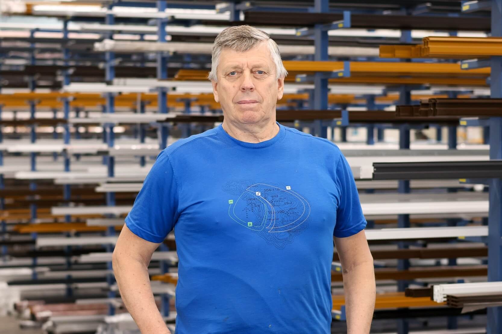 Ein Mann in blauem T-Shirt steht in einem Lager vor Regalen mit Metallstangen.