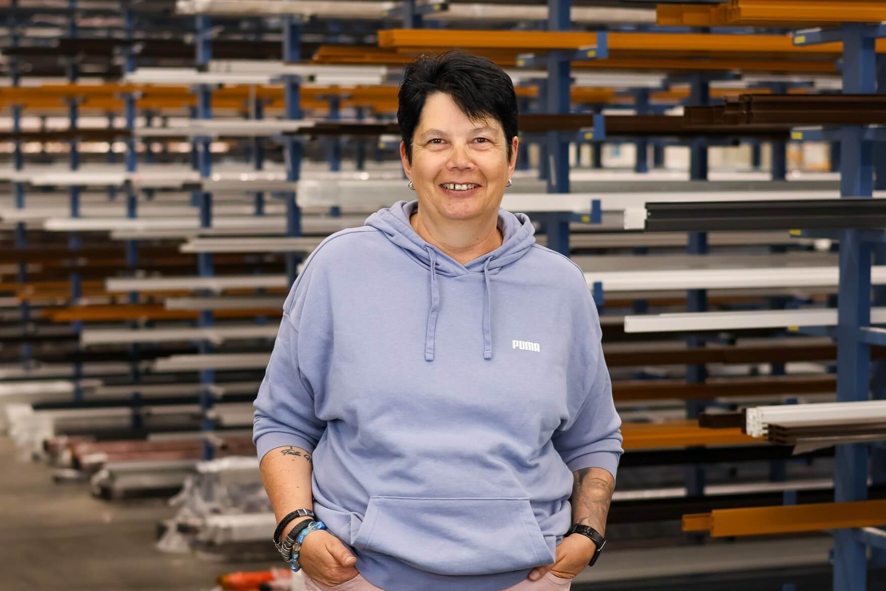 Frau mit kurzem Haar und Hoodie lächelt in einer Industriehalle