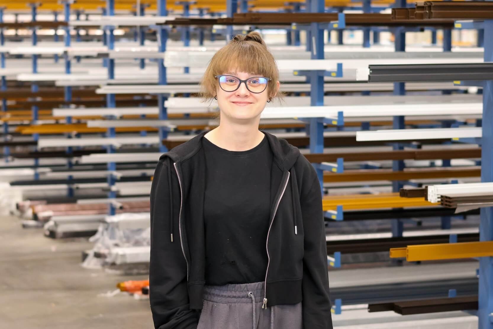 Person mit Brille in industriellem Umfeld vor Regalen
