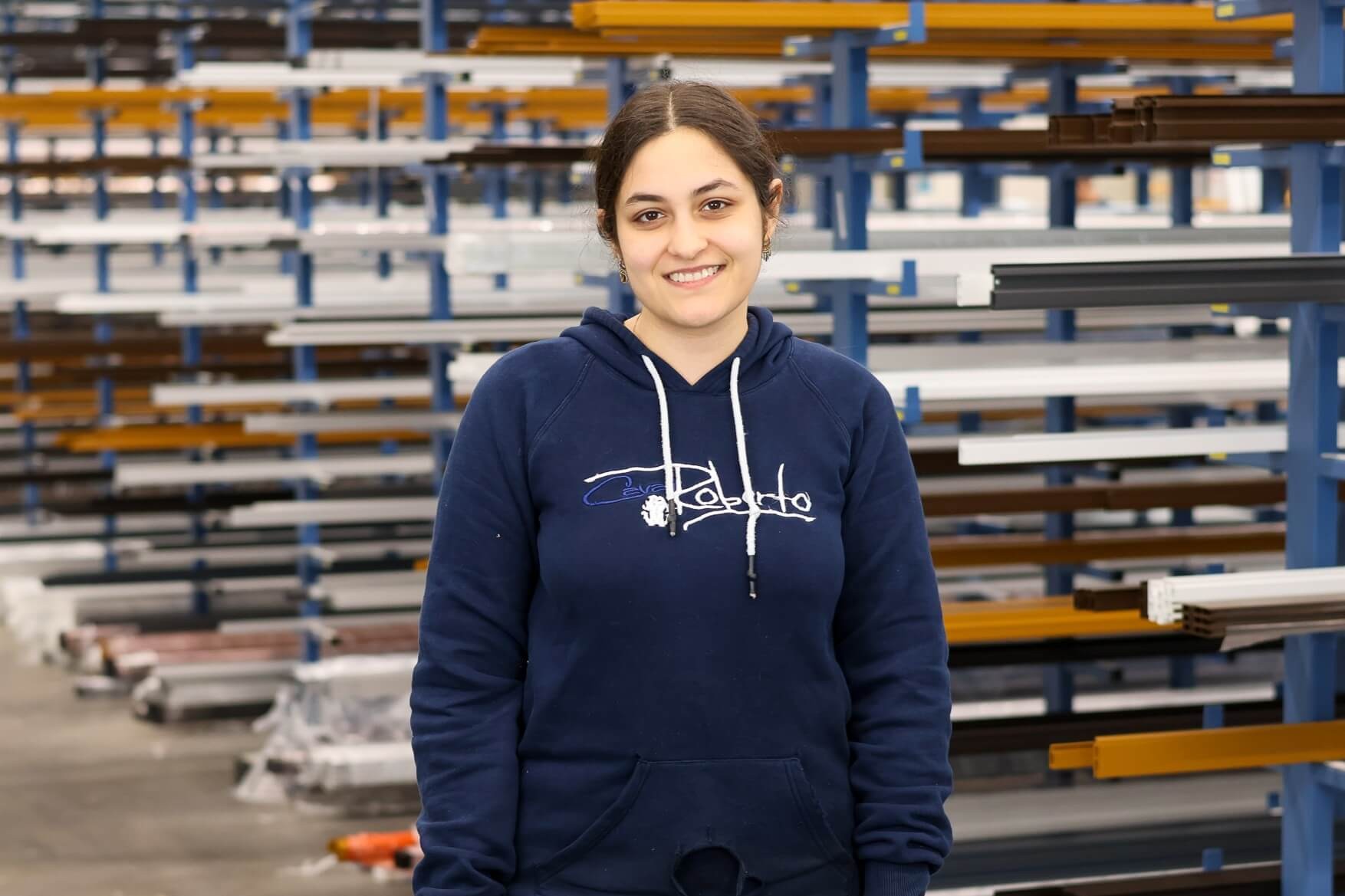 Junge Frau in blauer Kapuzenjacke lächelnd vor industriellem Hintergrund
