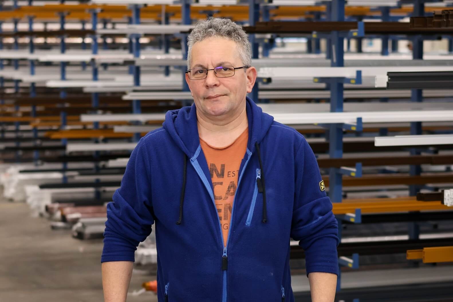 Arbeiter in einer Werkstatt mit blauem Oberteil vor Metallgestellen