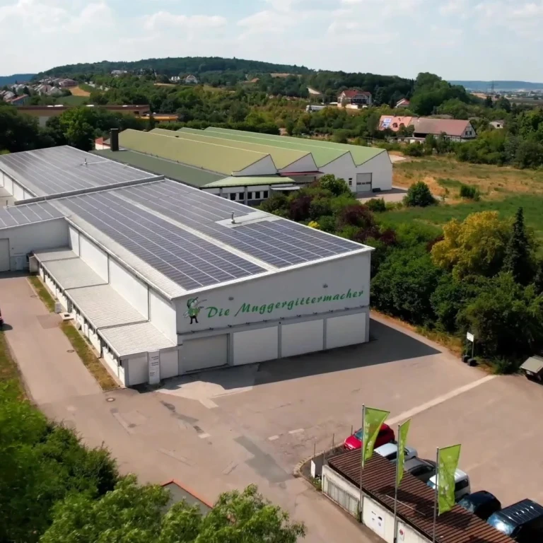 Firmengebäude von Die Muggergittermacher mit Solaranlage auf dem Dach, umgeben von Natur