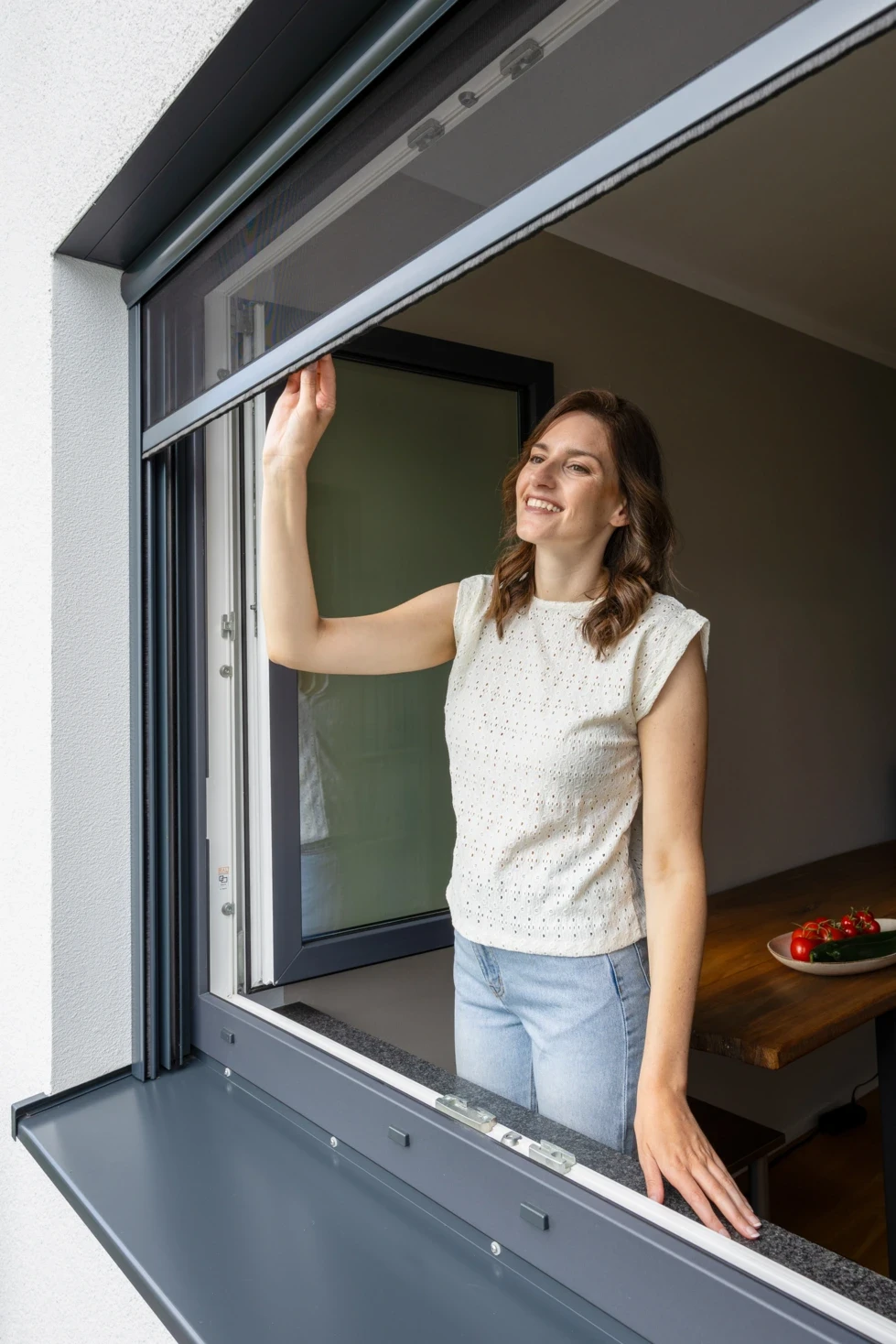 Frau öffnet ein Fliegengitter-Rollo an einem Fenster.
