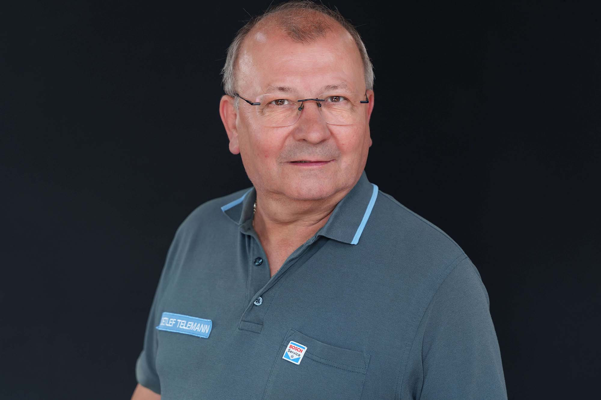 Porträt eines älteren Mannes mit Brille und Bosch Service Shirt vor schwarzem Hintergrund
