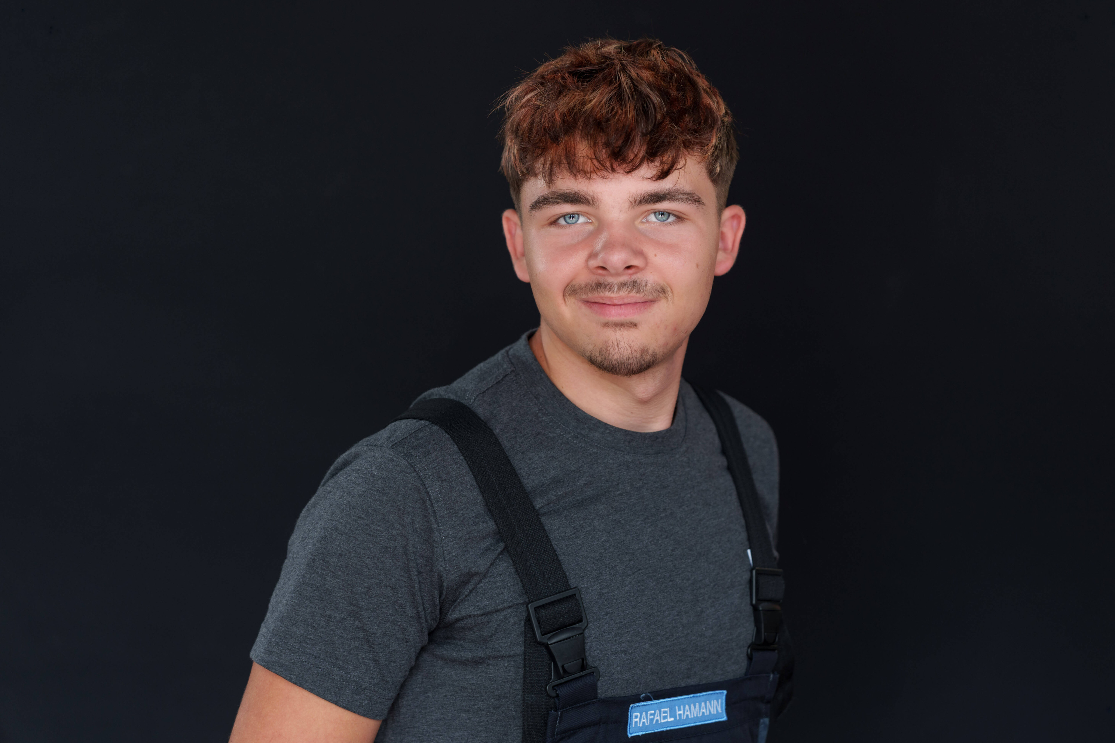 Porträt eines jungen Mannes mit braunen Haaren und grauem Shirt vor schwarzem Hintergrund