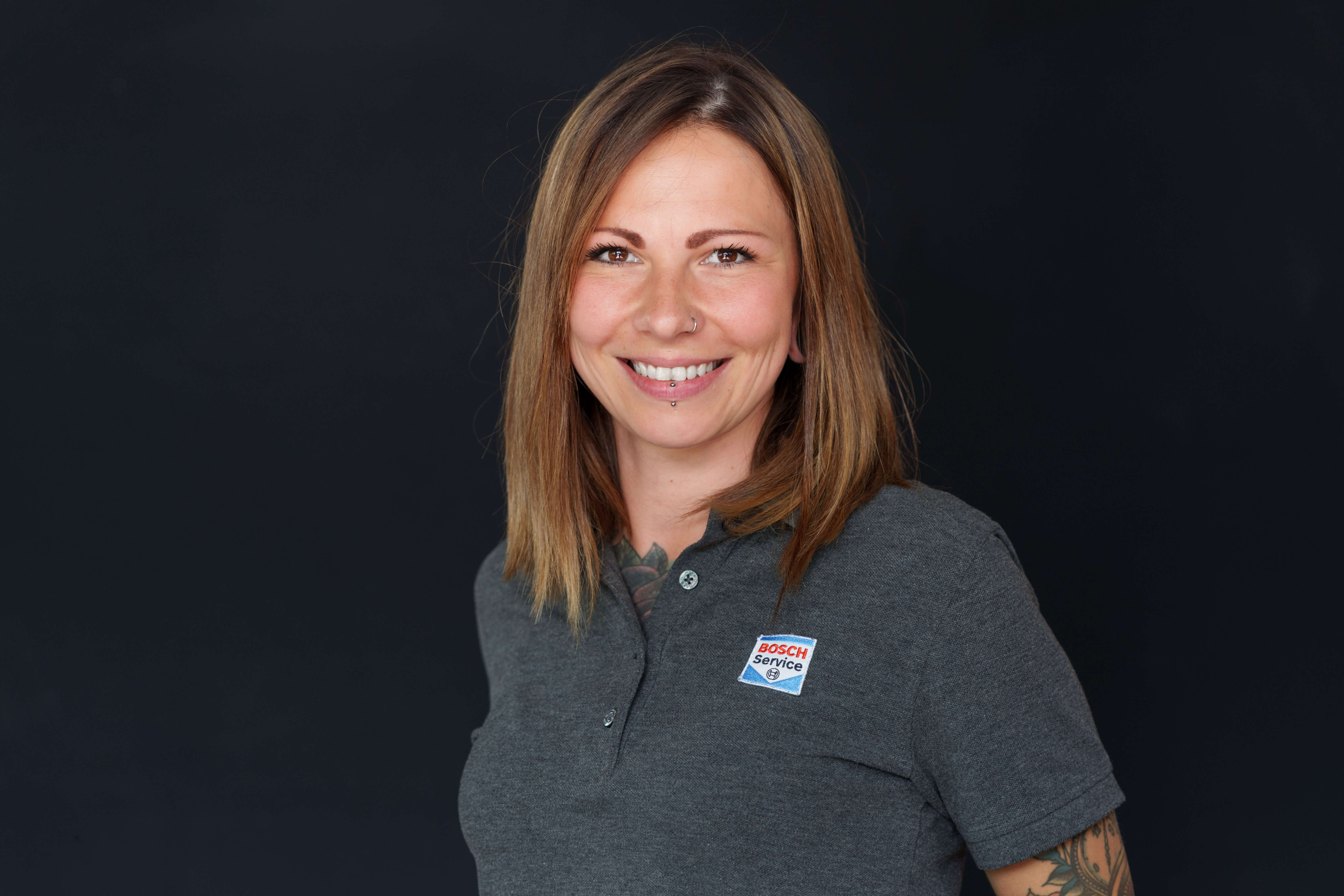 Porträt einer lächelnden Frau im Bosch Service Shirt vor dunklem Hintergrund