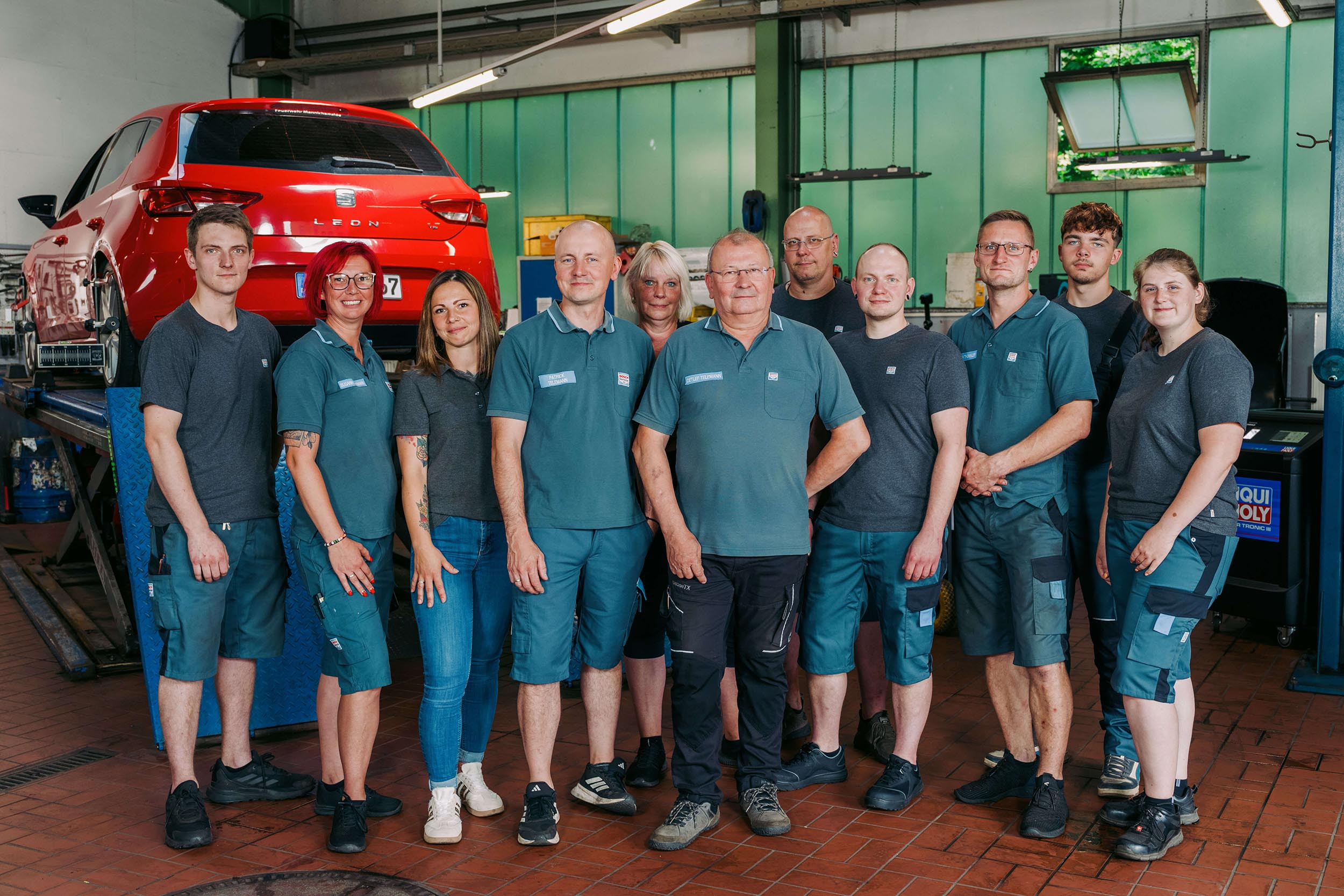 Teamfoto einer Autowerkstatt mit Mitarbeitern vor einem roten Seat Leon in der Werkstatt