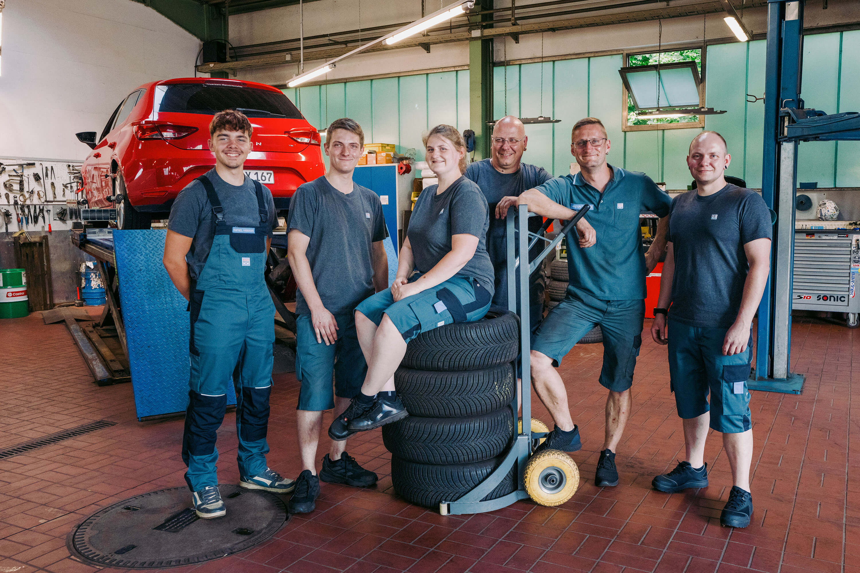 Team von Kfz-Mechanikern in einer Autowerkstatt mit Reifen und Auto im Hintergrund