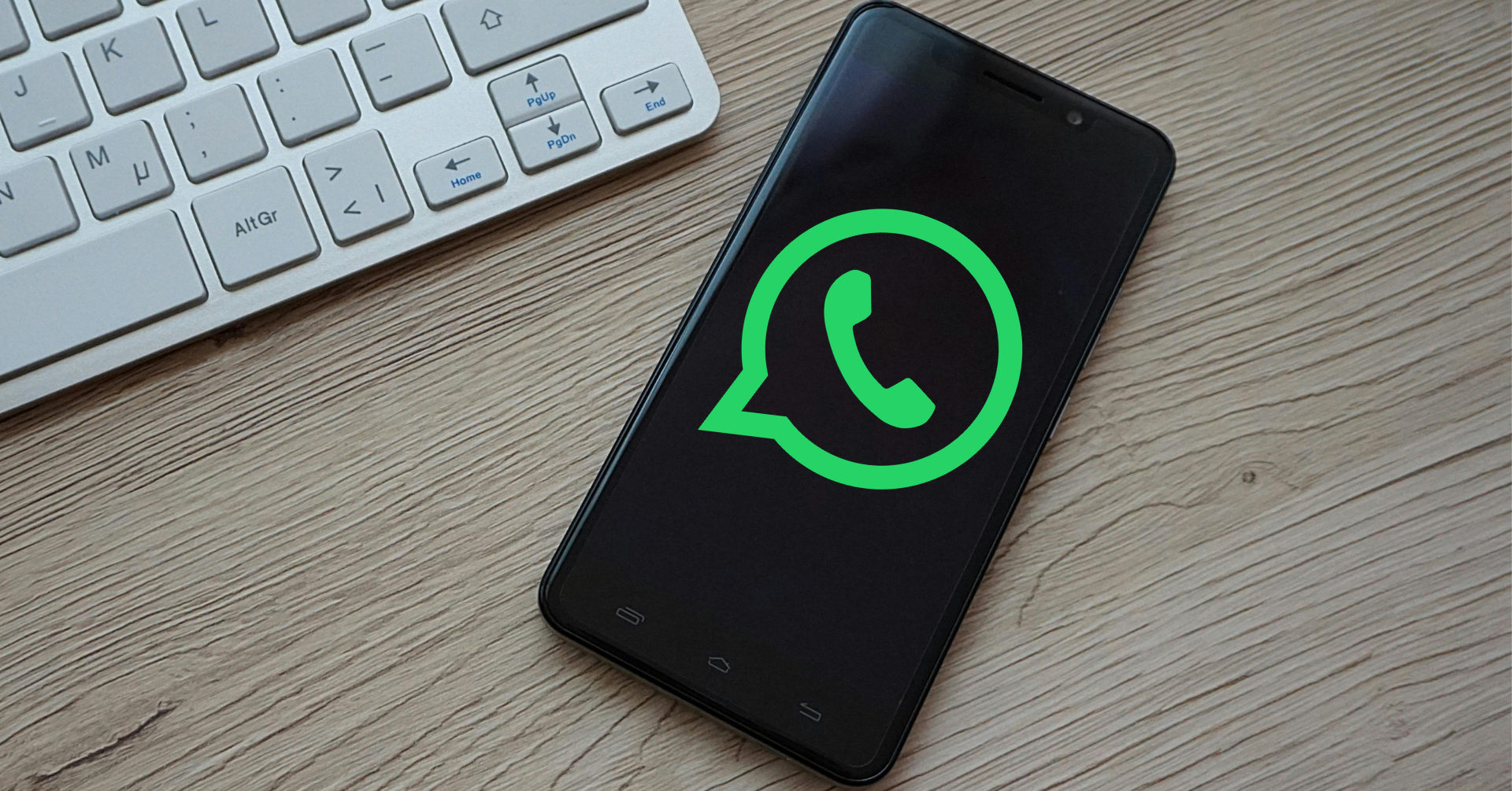 WhatsApp Logo auf Smartphone neben Tastatur