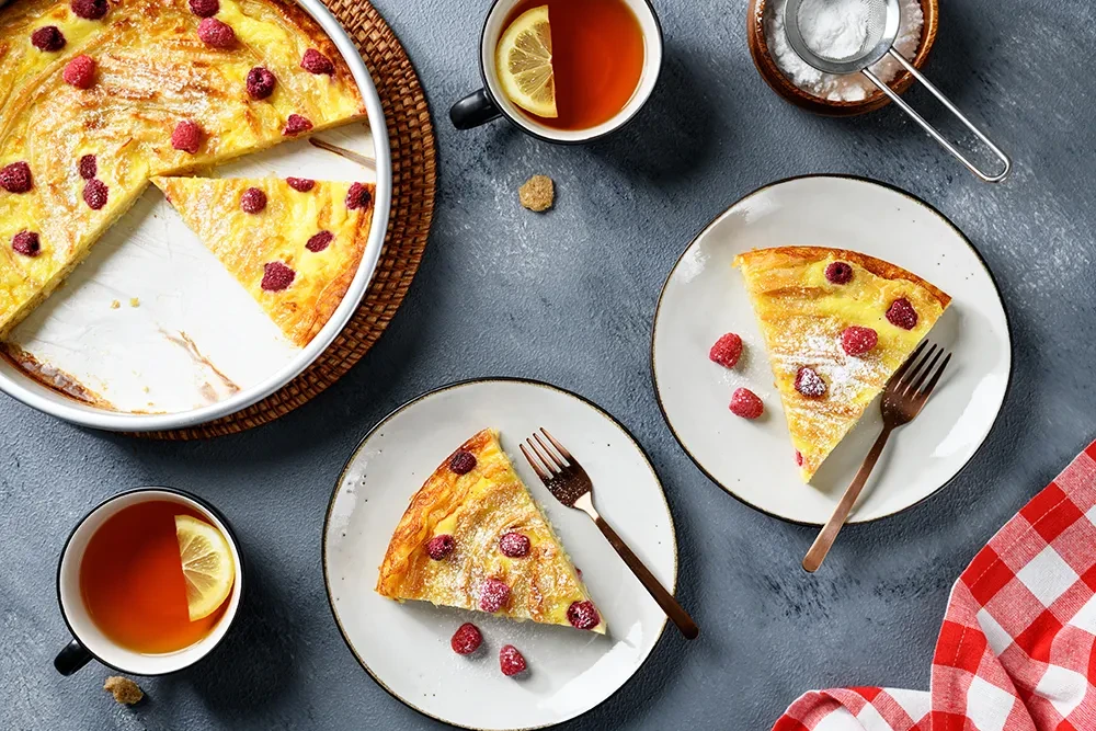 Himbeer-Kuchen und Tee als Inspiration für Backrezepte Himbeer-Kuchen auf Tellern mit Tee und Zitronenscheibe