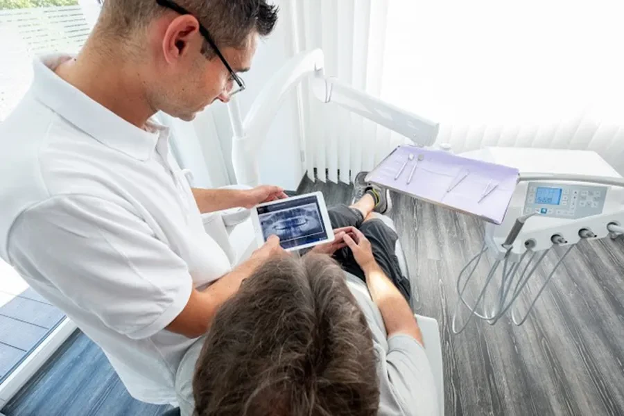 Moderne Zahnmedizin: Zahnarzt zeigt Patienten digitales Röntgenbild auf Tablet