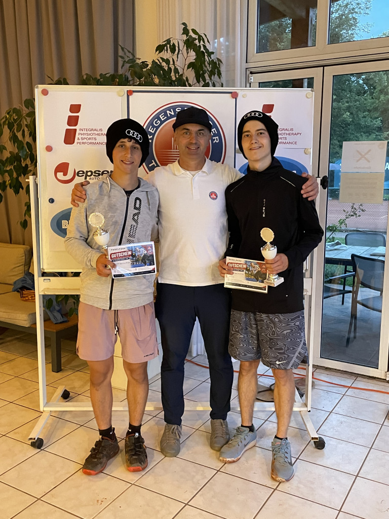 Siegerfoto mit zwei jungen Tennisspielern und einem Trainer nach einem Turnier, beide Spieler halten Pokale und Gutscheine in den Händen