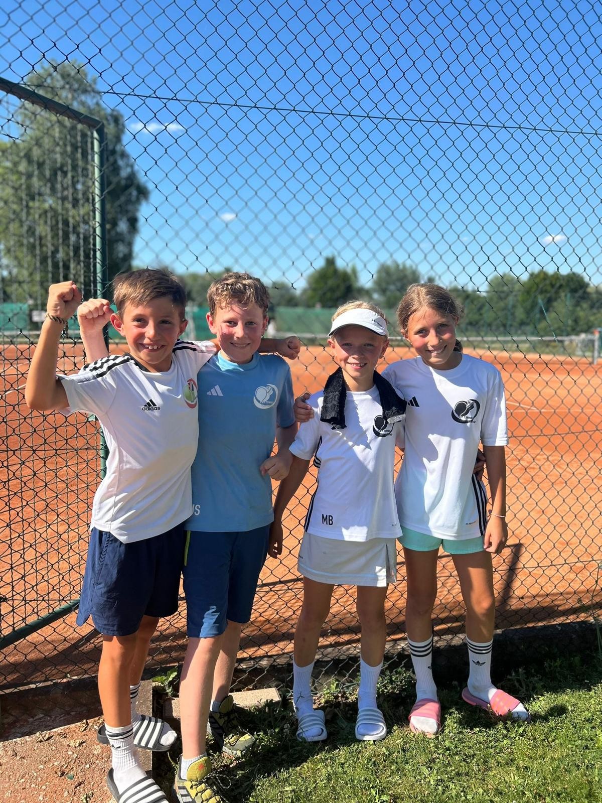Vier Kinder beim Tennistraining auf einem Sandplatz im Sommer