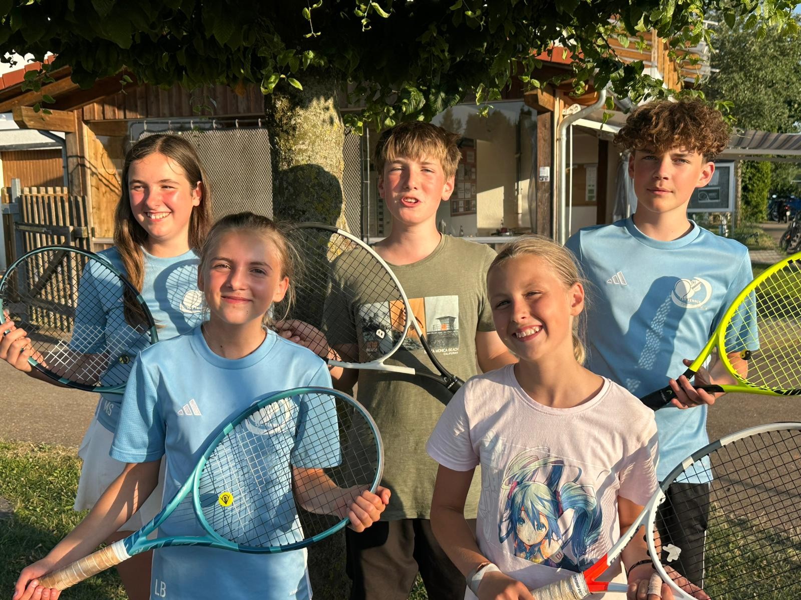 Fünf Jugendliche im Sommer mit Tennisschlägern unter einem Baum.