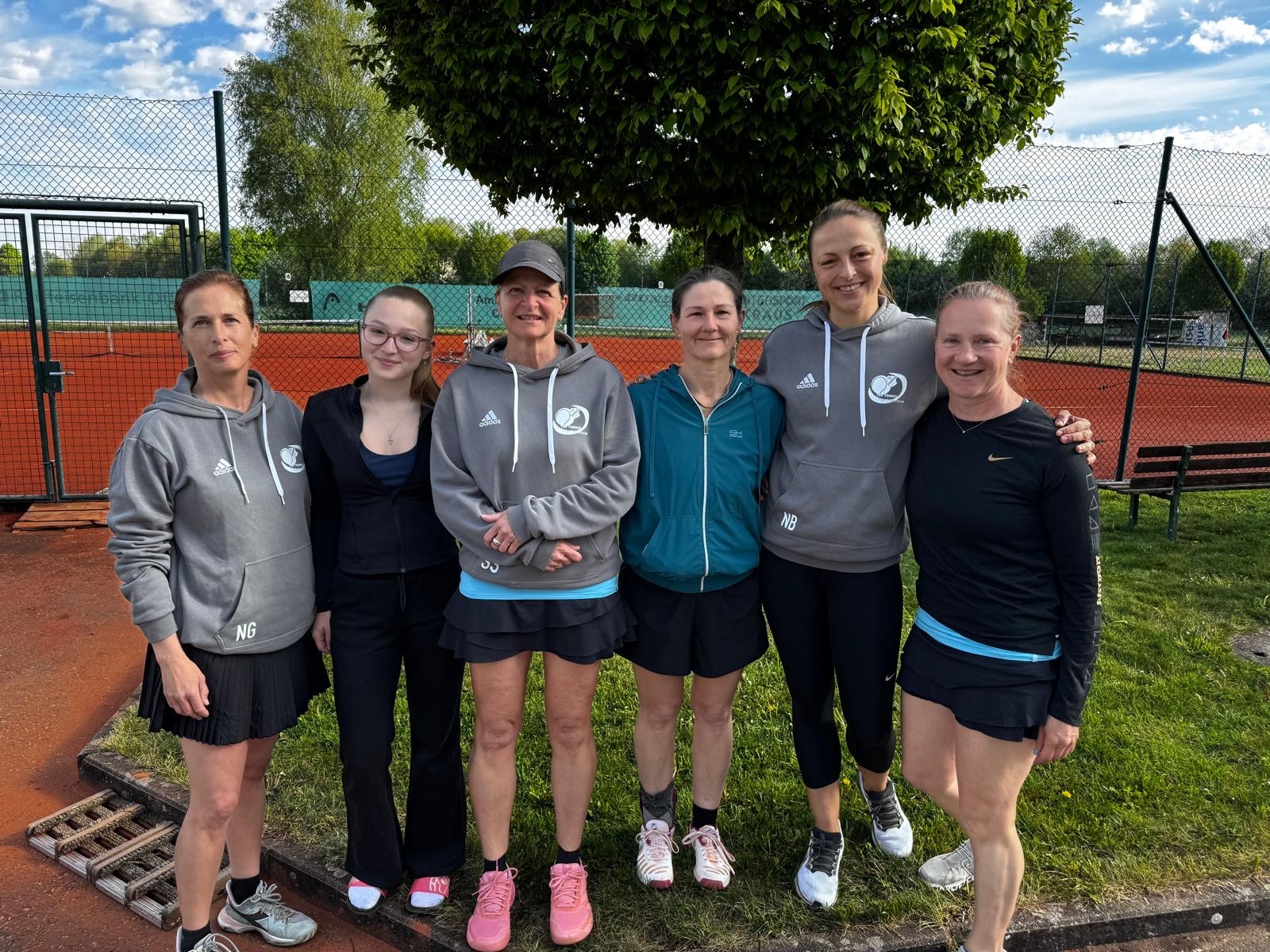 Damen-Tennismannschaft auf Tennisplatz im Freien vor Baum und Netz