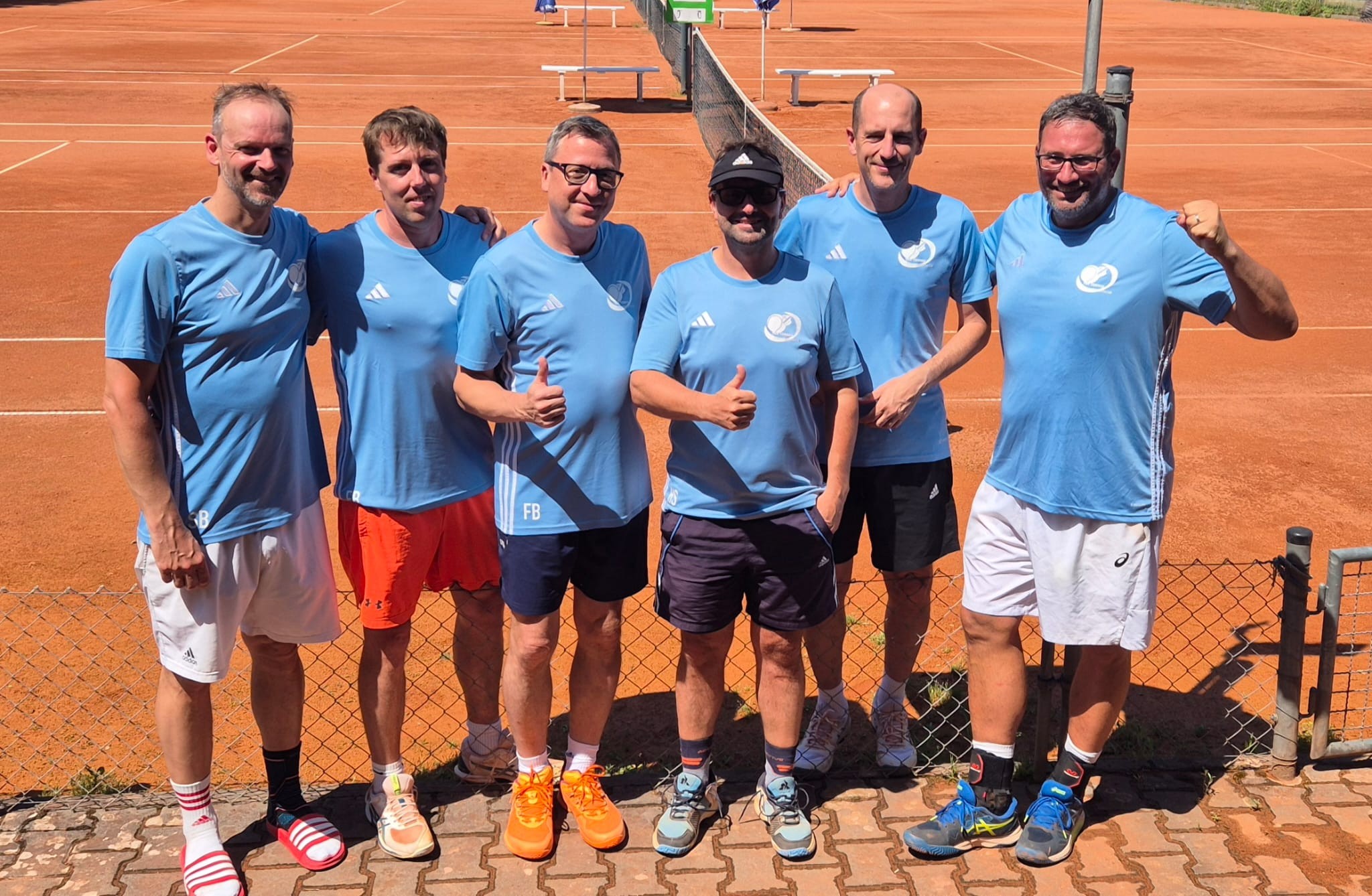 Sechs Männer im blauen Trikot auf einem Tennisplatz, Gruppenfoto bei sonnigem Wetter