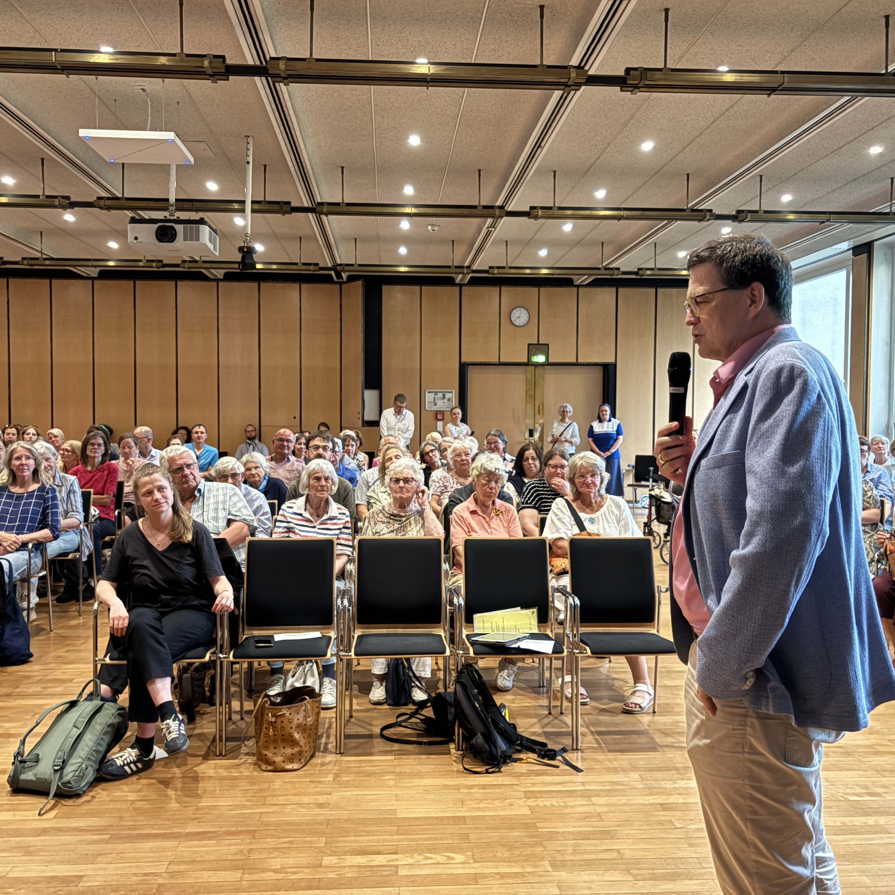 Vortragender Mann mit Mikrofon spricht vor großem Publikum in einem modernen Konferenzraum