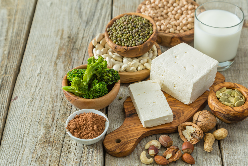 Verschiedene pflanzliche Proteinquellen wie Tofu, Nüsse und Hülsenfrüchte auf einem Holztisch