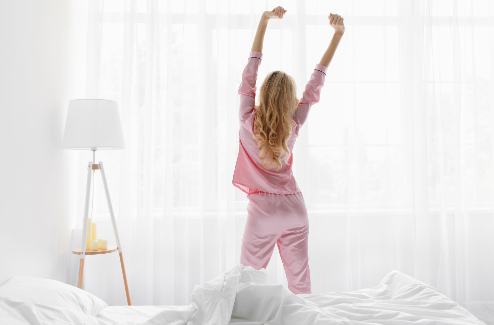 Frau in rosa Pyjama streckt sich am Morgen im Schlafzimmer