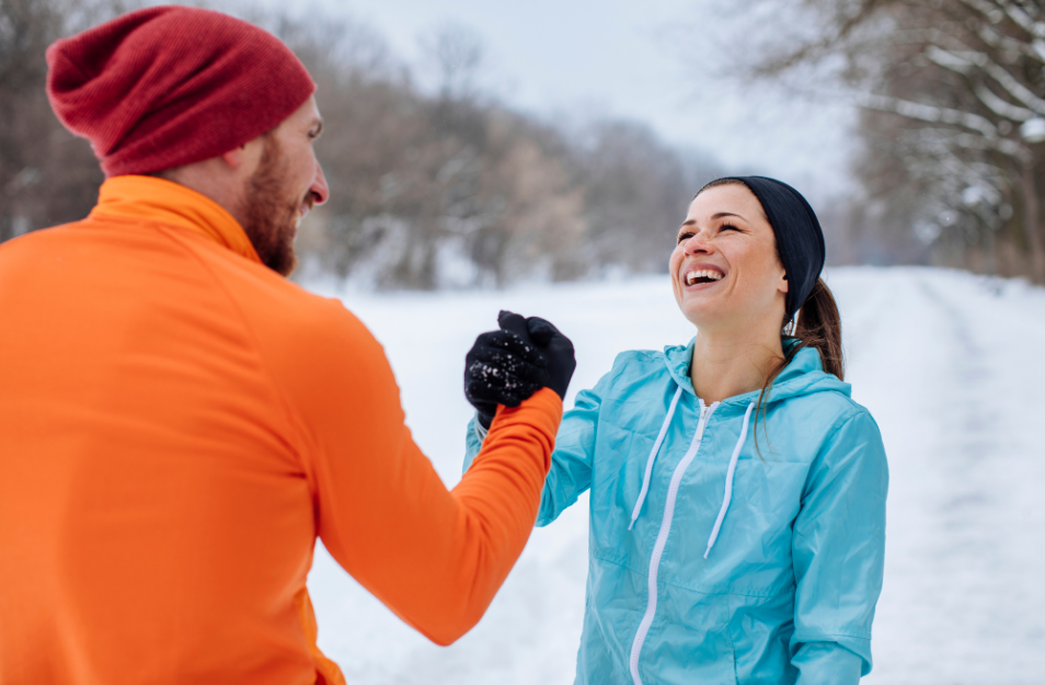 Zwei Menschen in Sportkleidung begrüßen sich im verschneiten Park mit Handschlag