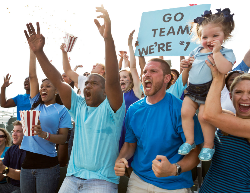 Jubelnde Fans bei einem Sportevent mit einem Schild 'Go Team, We're #1'