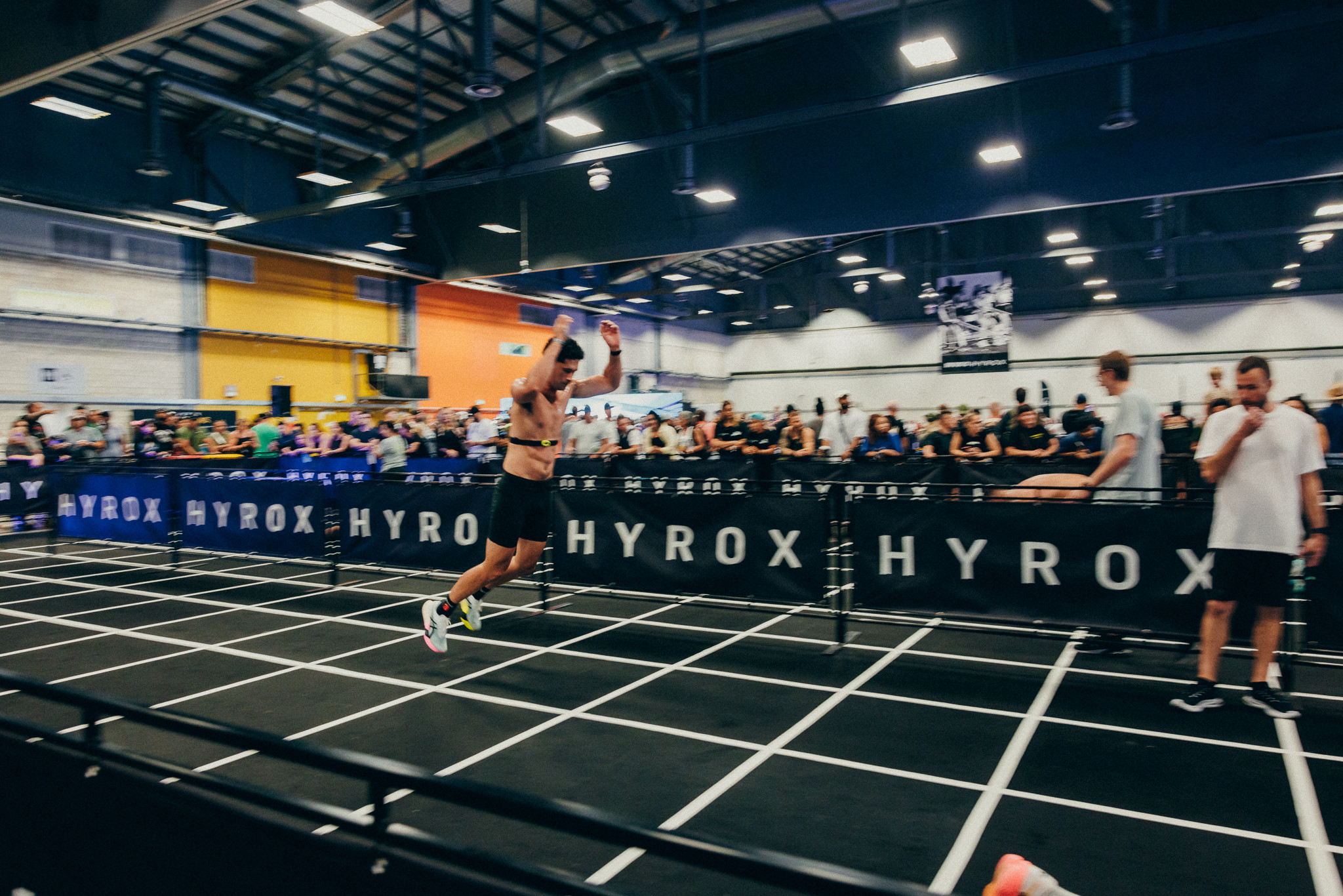 Sportler beim HYROX Wettkampf in einer Halle, springend auf einer markierten Bahn