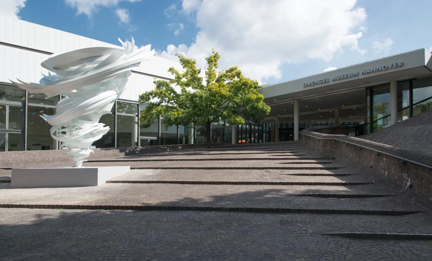 Eingang des Sprengel Museums mit moderner Skulptur und Baum im Vordergrund