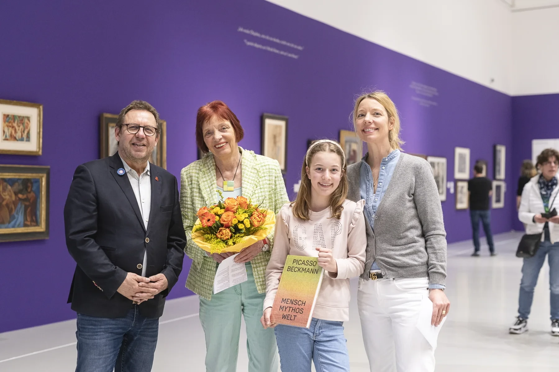 Gruppenfoto vor lila Wand in einer Ausstellung zu Pablo Picasso, eine Person hält ein Buch mit dem Titel 'Picasso Beckmann Mensch Mythos Welt'