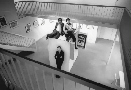 Schwarzweiß-Fotografie mit Peter Gauditz in einer modernen Galerie, drei Personen posieren auf und an einer Wandinstallation.