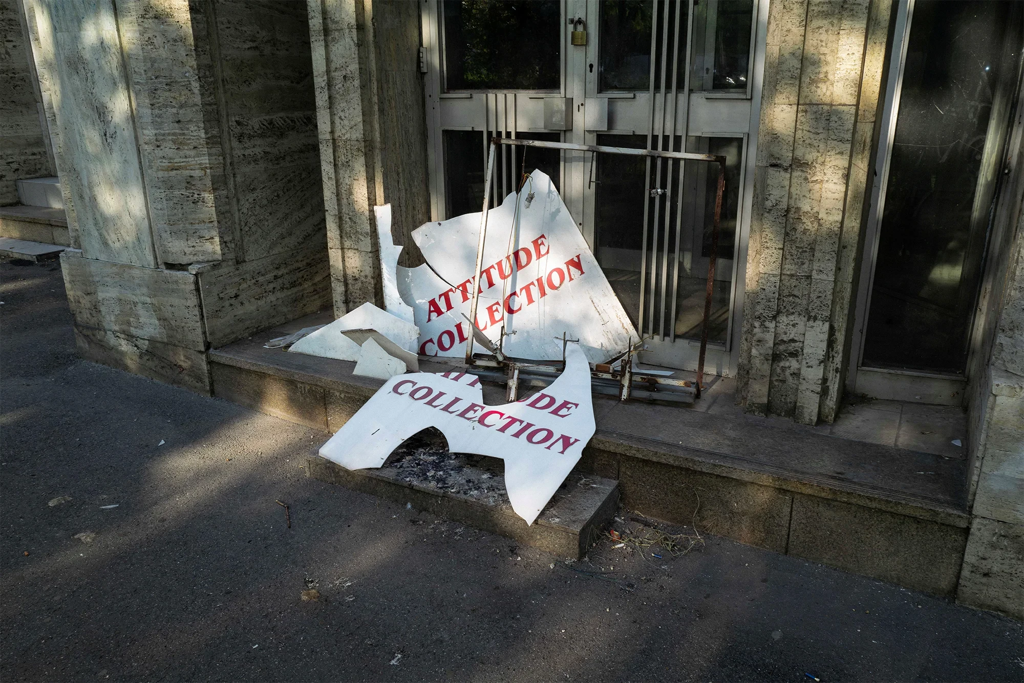 Zerbrochenes Schild mit der Aufschrift 'Attitude Collection' vor einem Gebäude – Beitrag Archiv Sven Julien Kanclerski