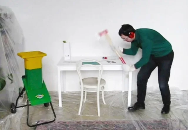 Bastian Hoffmann zerstört mit einem Hammer einen weißen Tisch in einem Atelierraum