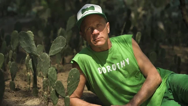 Björn Melhus aus Spectral Afterlives in grünem Shirt mit Aufschrift Dorothy, sitzend zwischen Kakteen