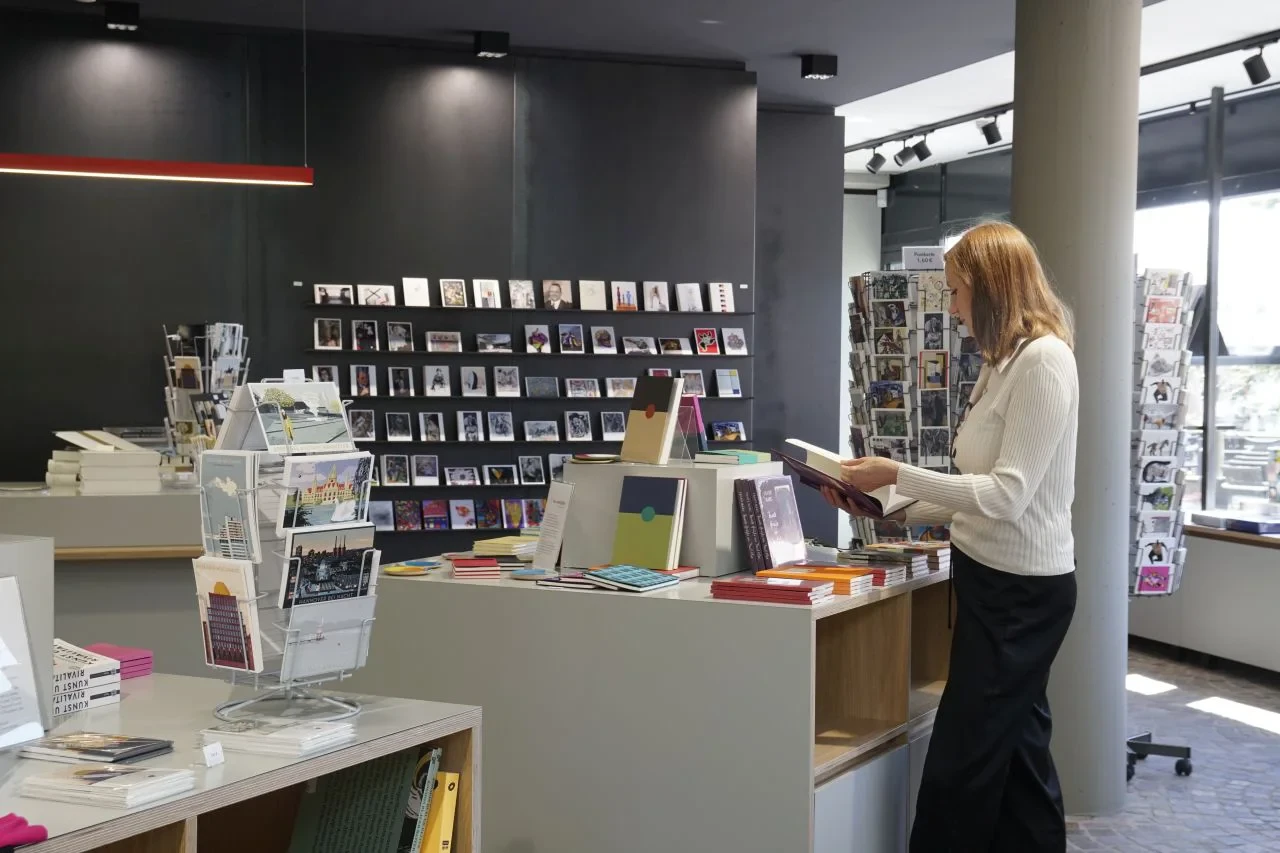 S-Shop Raumansicht mit Postkarten, Büchern und einer Frau beim Stöbern, Foto von Sarah Jade