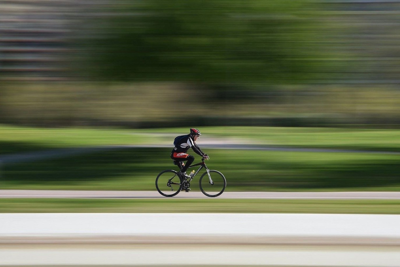 Unterwegs mit dem Rennrad Prostatahilfe Deutschland: Ein Rennradfahrer fährt auf einem Radweg, vor einem grünen Hintergrund (Tiefenunschärfe).