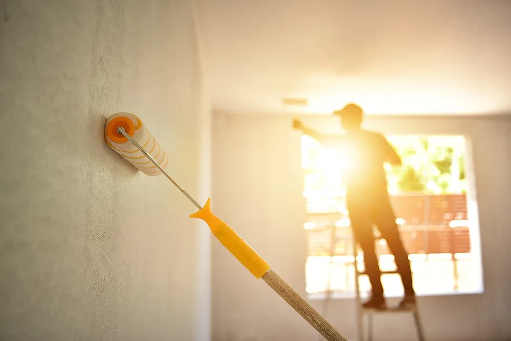 Malerarbeiten und Renovierung: Wand streichen mit Farbrolle bei Sonnenlicht Maler streicht eine Wand mit Farbrolle bei Sonneneinfall, Renovierungsarbeiten im Innenraum