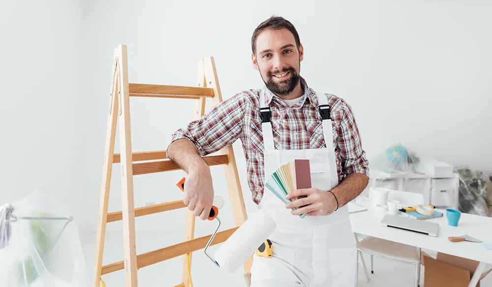 Maler bei der Arbeit mit Farbroller und Farbmuster vor einer Leiter