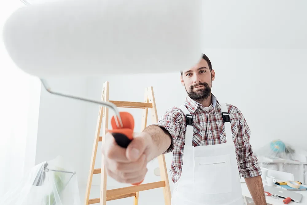 Maler streicht mit Farbrolle eine Wand, im Hintergrund eine Leiter