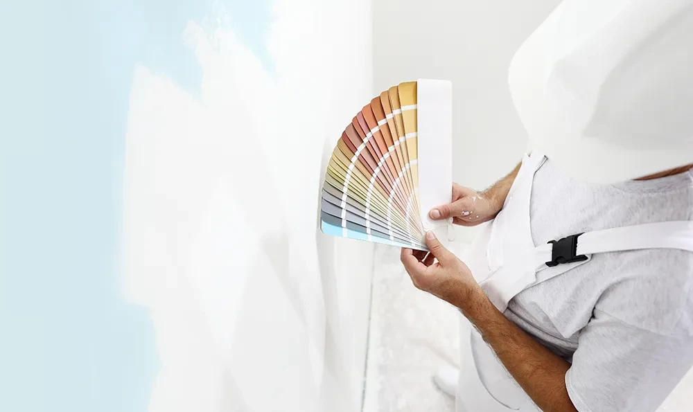 Maler hält Farbpalette vor weißer Wand zur Farbauswahl