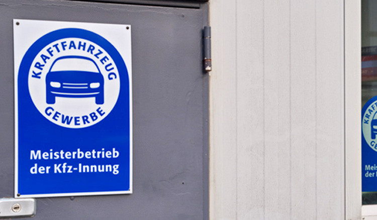 Eingangstür eines KFZ-Meisterbetriebs mit blauem Innungs-Schild